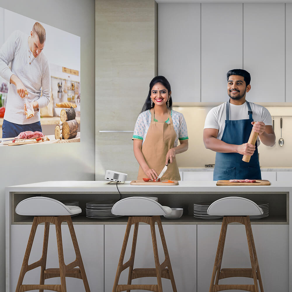 Couple cooking in a modern kitchen while watching a chef tutorial on an ultra short throw projector — ideal for compact spaces and kitchen use without screen shadows.